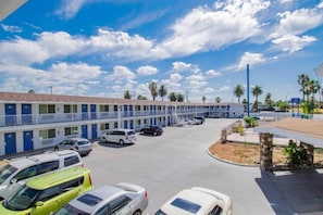 A motel with multiple rooms, a parking lot, and a clear sky. - 2 QUEEN BEDS | SMOKING, MINI FRIDGE (San Bernardino)