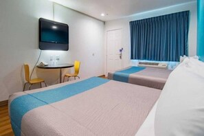 Habitació d'hotel amb dos llits, una taula de treball, cadires, televisió i una finestra amb cortines.