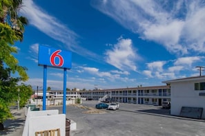 Un motel con un llamativo letrero azul que muestra el número 6, un estacionamiento con varios coches y una hilera de edificios del motel al fondo.