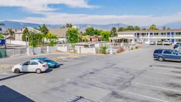 A parking lot with several cars, a building with a flat roof, and mountains in the background.