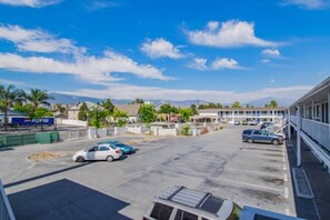 Un aparcament amb diversos cotxes, un edifici amb un balcó i un cel blau clar.