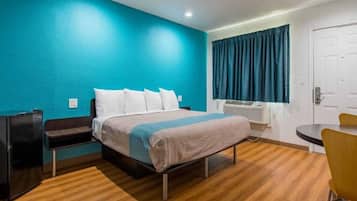 Una habitación de hotel con cama, escritorio, silla y ventana con cortinas.