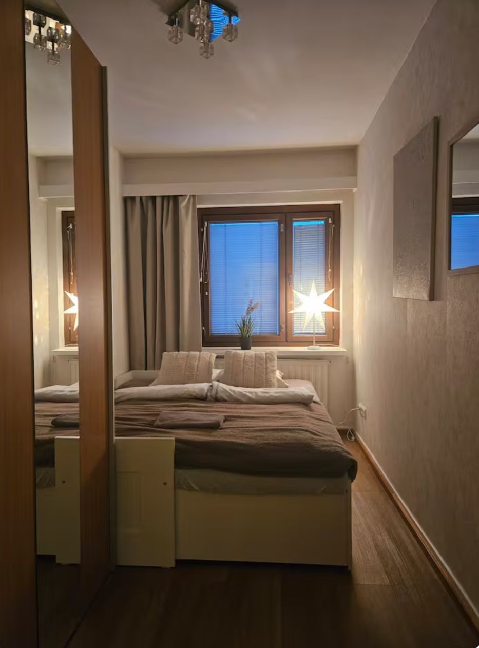 Ein Schlafzimmer mit einem Bett, einem Fenster mit Vorhängen, einer sternförmigen Lampe und einem Spiegel an der Wand.