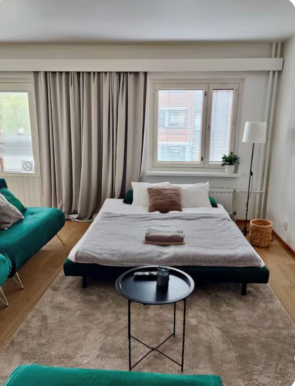 Une chambre à coucher avec un lit, une table de chevet, une chaise, une fenêtre avec des rideaux et une plante en pot.