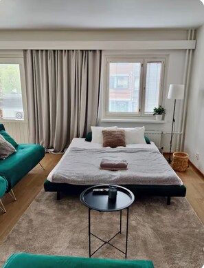Een slaapkamer met een bed, nachtkastje, stoel, raam met gordijnen en een potplant.