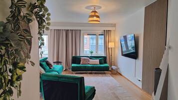 A modern living room with green sofas, a flat-screen TV, and a hanging plant.