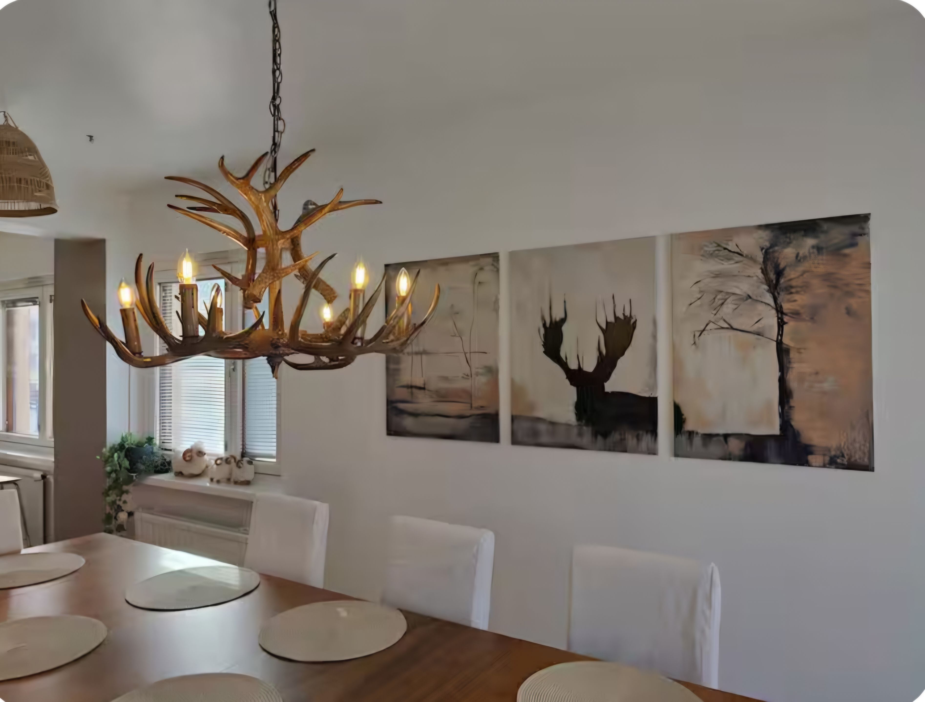 Un espace repas agrémenté d’un lustre, de chaises blanches et d’œuvres d’art accrochées au mur.