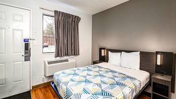 A hotel room with a bed, a window with curtains, an air conditioning unit, and a door with a security lock.