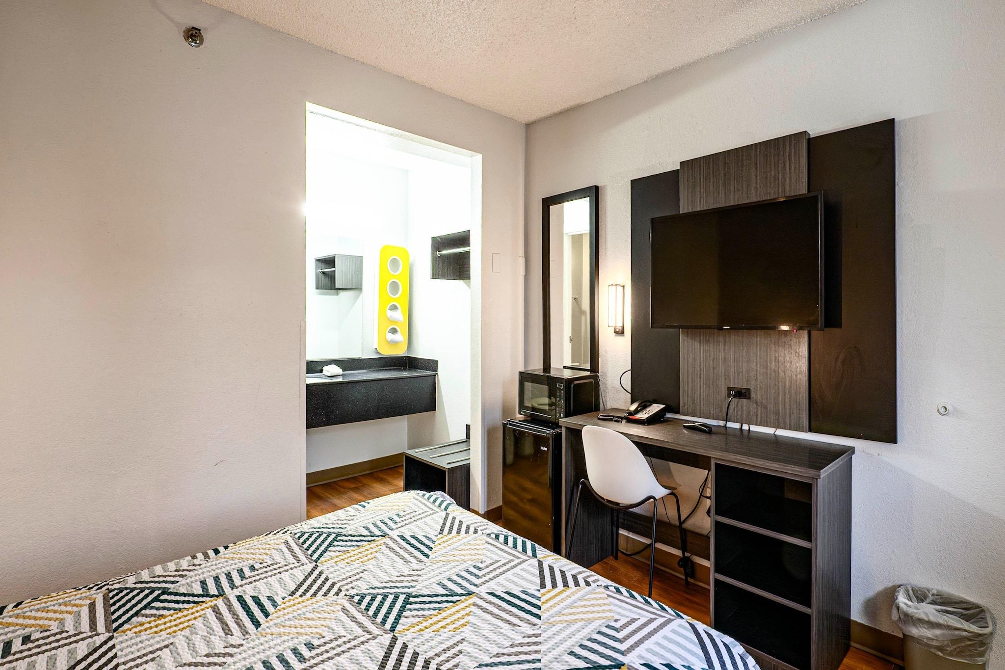 A bedroom with a bed, a desk, a chair, a television, and a bathroom visible through an open door.