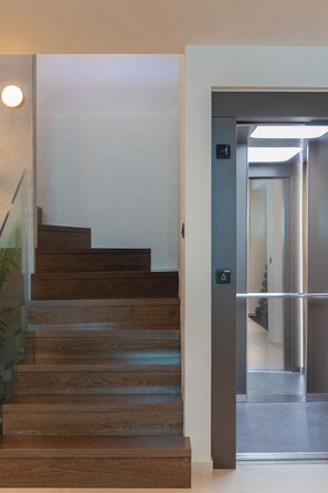 Ein modernes Interieur mit einer Holztreppe, einer Glastür des Aufzugs und einer gut sichtbaren Aufzugszahl.