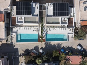 Ein Wohngebäude mit zwei Schwimmbecken, Solaranlagen und einem Parkplatz mit Autos.