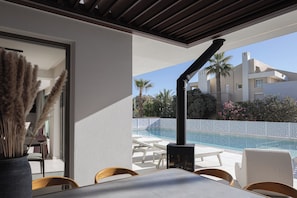 Ein Poolbereich im Freien mit Liegestühlen und einem Tisch, Blick auf ein Gebäude mit Pool sowie eine Pergola.