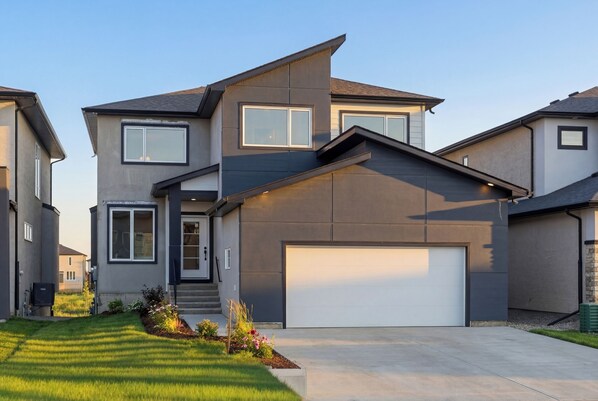 A modern two-story house with a garage, a well-maintained lawn, and a clear sky.
