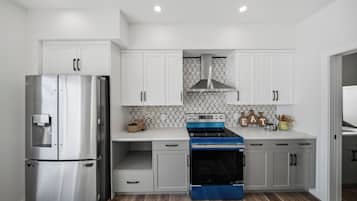 Uma cozinha moderna com eletrodomésticos de aço inoxidável, armários brancos e painel de azulejos em padrão herringbone.