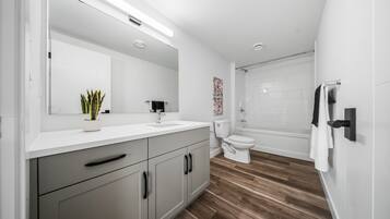 A modern bathroom with a white vanity, a sink, a toilet, and a shower area.