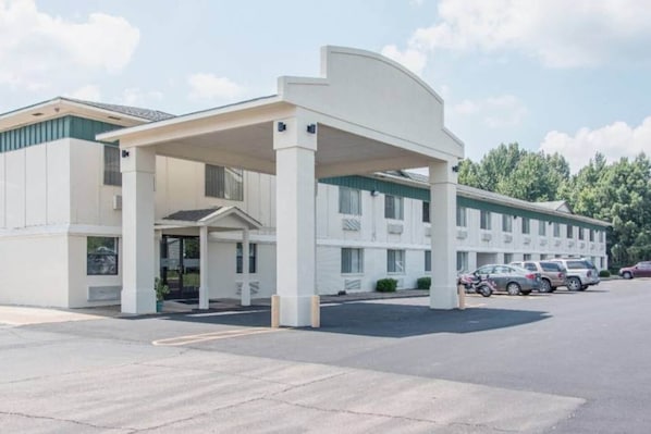 A motel with a covered entrance, multiple parking spaces, and a row of parked cars.