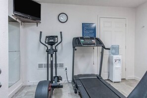 A fitness center with an elliptical machine, a treadmill, a water dispenser, and a clock on the wall.