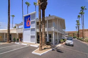 Un motel con un llamativo letrero azul, estacionamiento y palmeras.