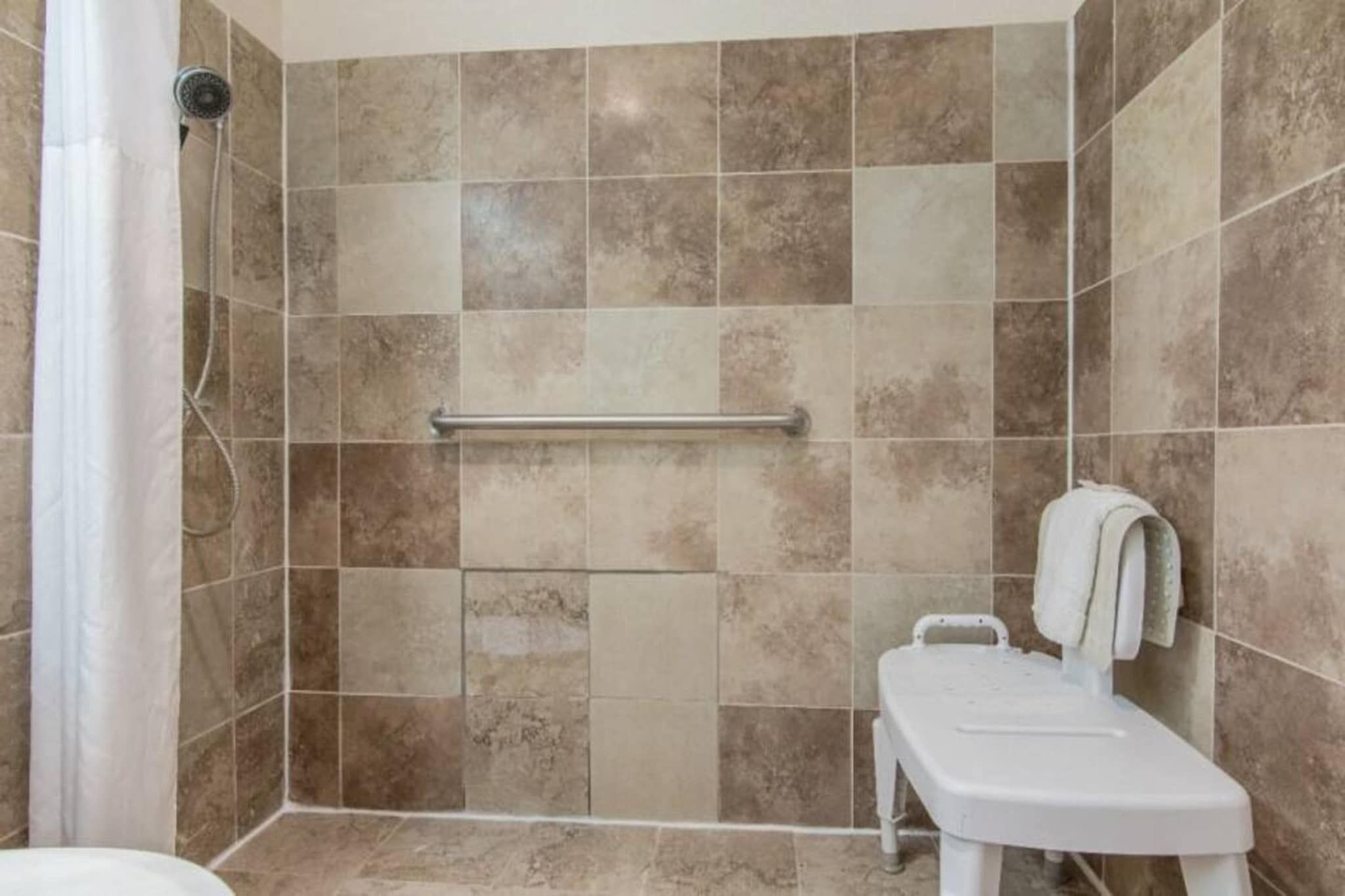 Un área de ducha con pasamanos, un inodoro blanco y una toalla colgada en la pared.