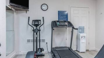 A fitness center with an elliptical machine, a treadmill, a water dispenser, and a clock on the wall.