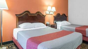A hotel room with two beds, each with a wooden headboard, white bedding, and a red and grey blanket. There are two bedside lamps and a telephone on the nightstand.