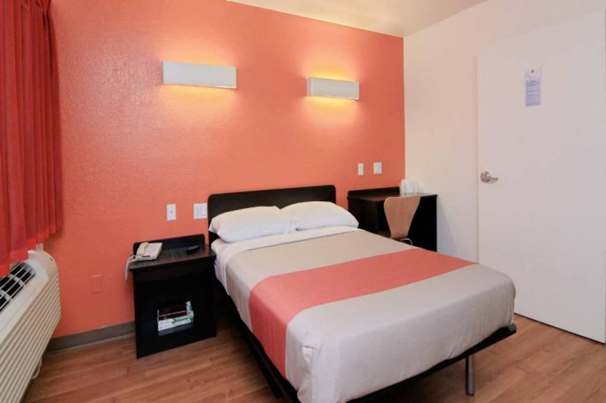 A hotel room with a bed, bedside tables, a heater, and a door.