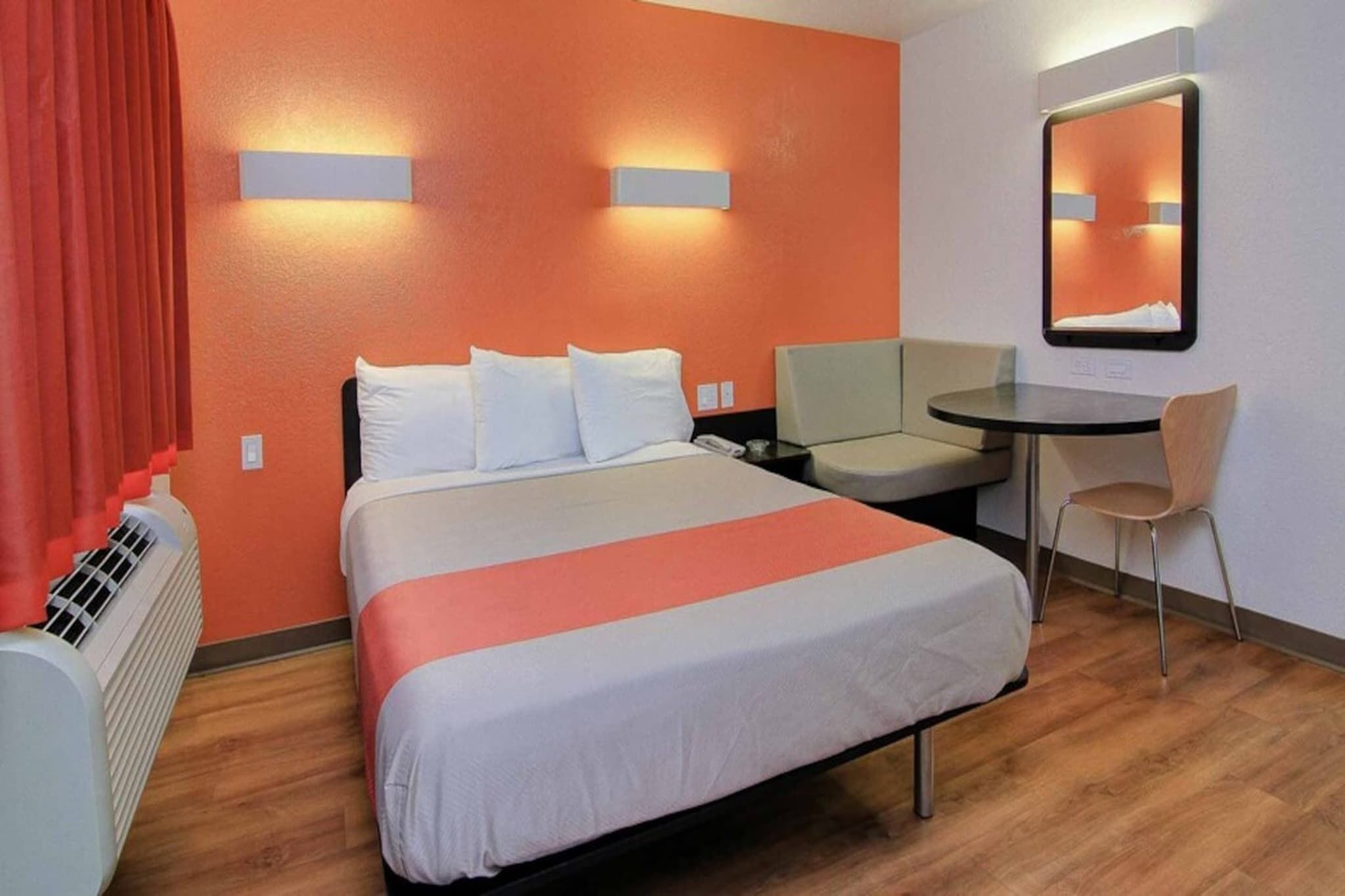 A hotel room with a bed, a desk, a chair, a heater, and a mirror.
