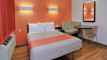 A hotel room with a bed, a desk, a chair, a heater, and a mirror.