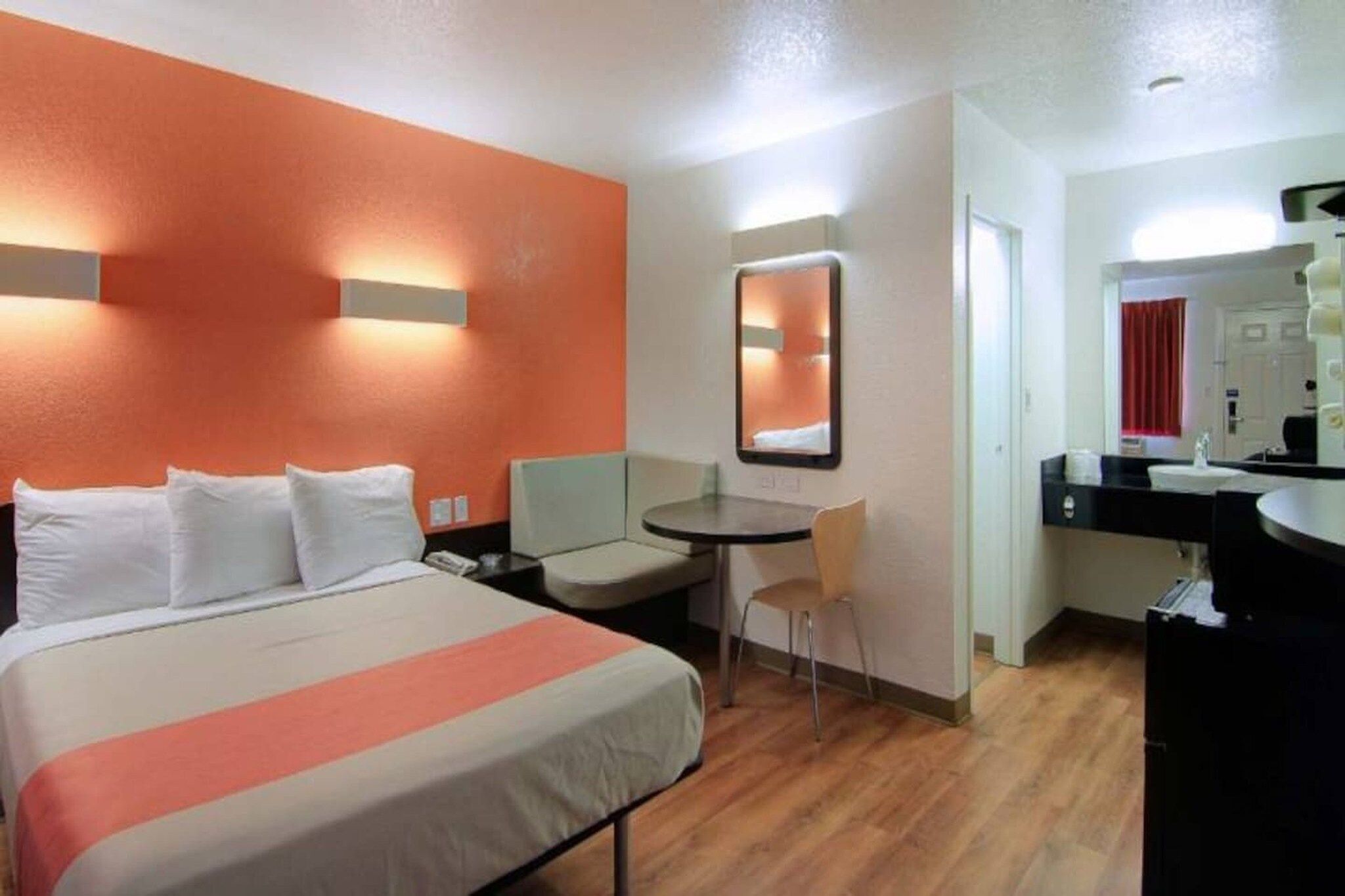 A hotel room with a bed, a desk, a chair, a round table, and a mirror.