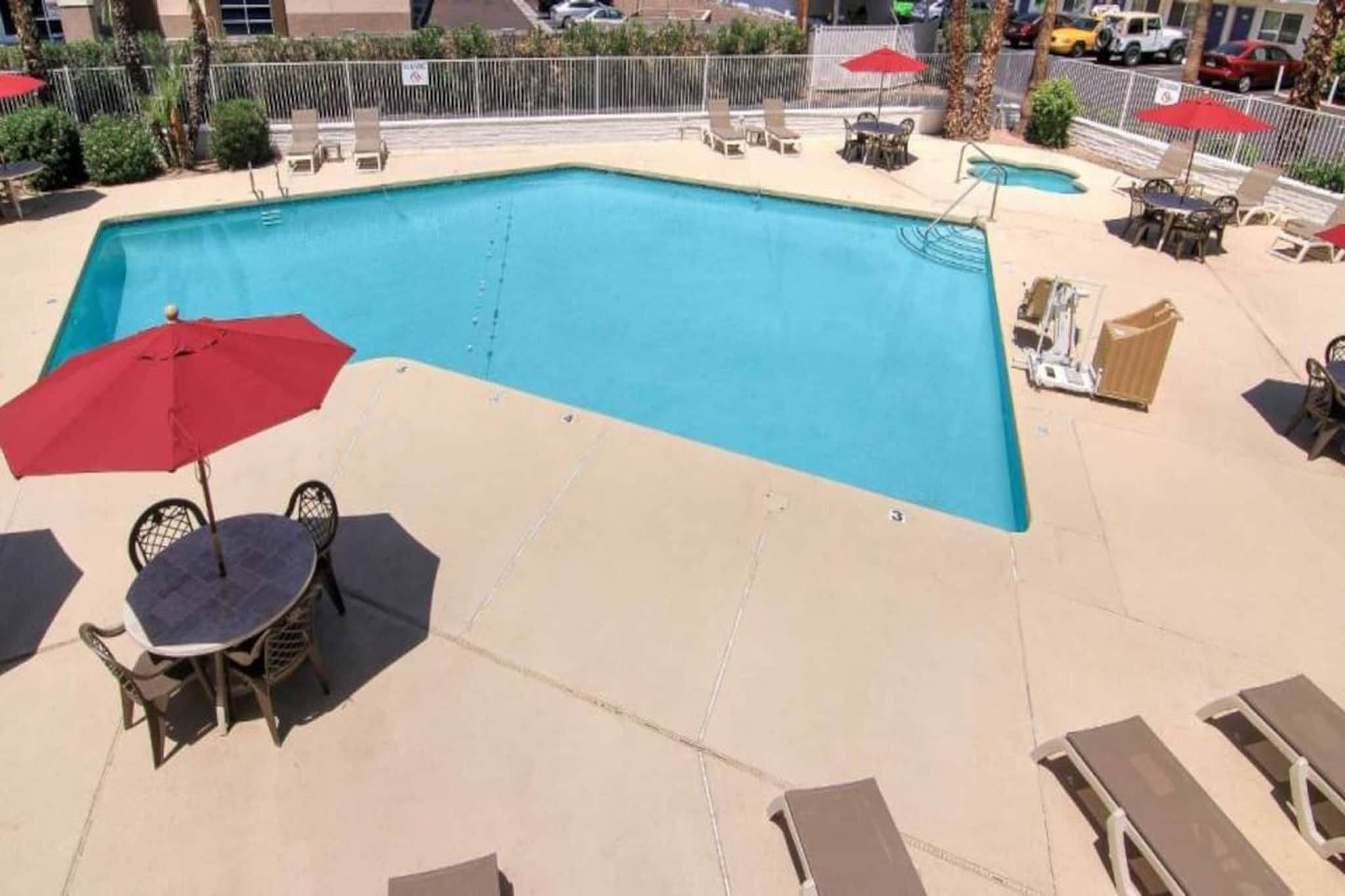 Une piscine entourée d’une clôture et de palmiers, avec des chaises longues et des parasols.