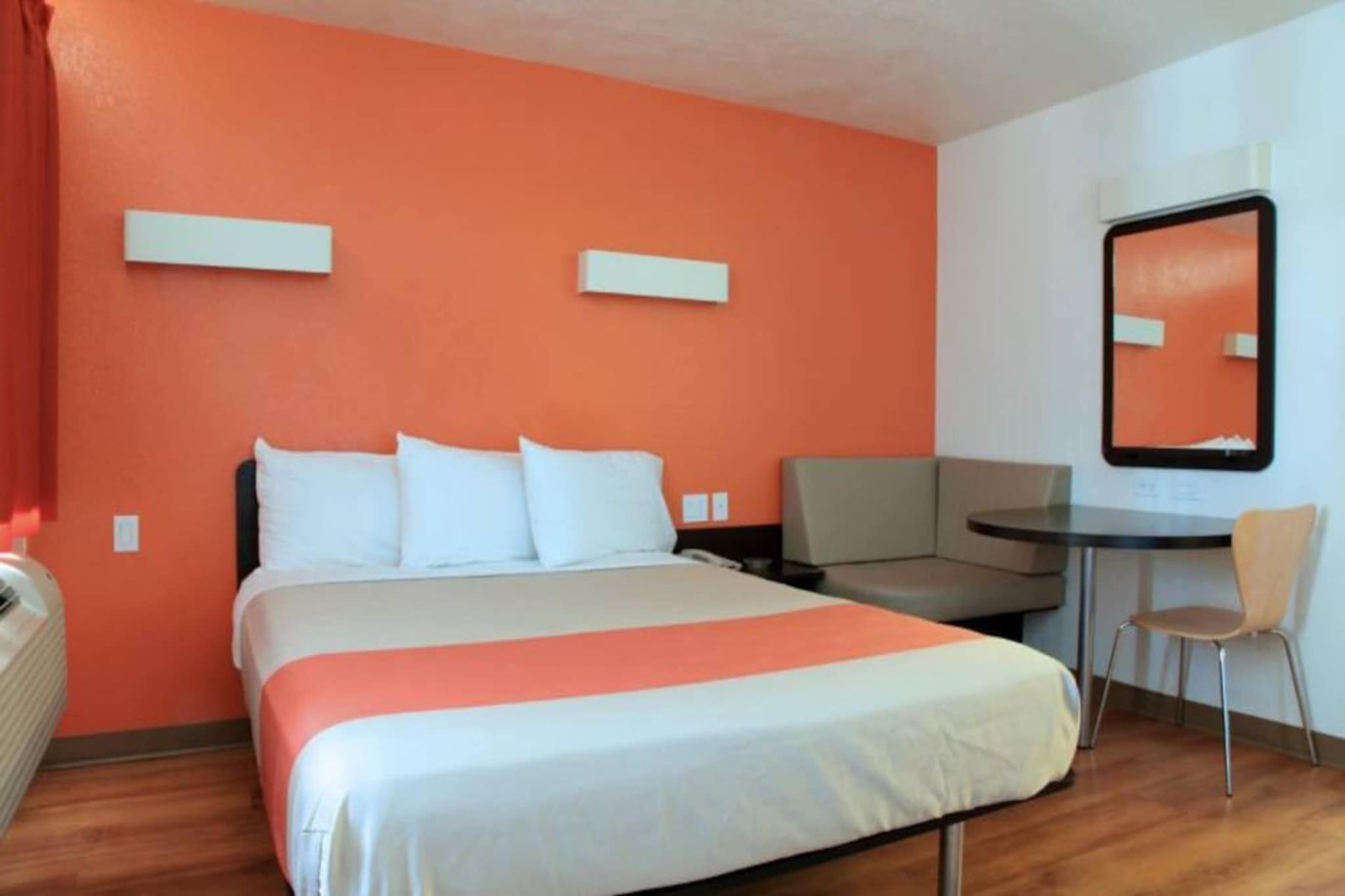 Une chambre d’hôtel avec un lit, un bureau, une chaise et un miroir au mur.