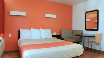 A hotel room with a bed, a desk, a chair, and a mirror on the wall.