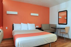 Une chambre d’hôtel avec un lit, un bureau, une chaise et un miroir au mur.