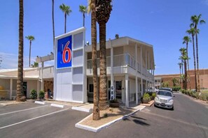 Un motel reconnaissable à son grand panneau indiquant le chiffre « 6 », un parking et des palmiers.