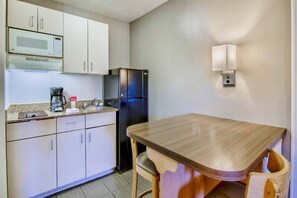 Una cocina compacta con armarios blancos, un refrigerador negro, microondas, cafetera y una mesa de madera con sillas.