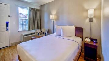 Habitación de hotel con una cama grande, dos lámparas de noche, un escritorio con silla, una ventana con cortinas y una puerta con cerradura.