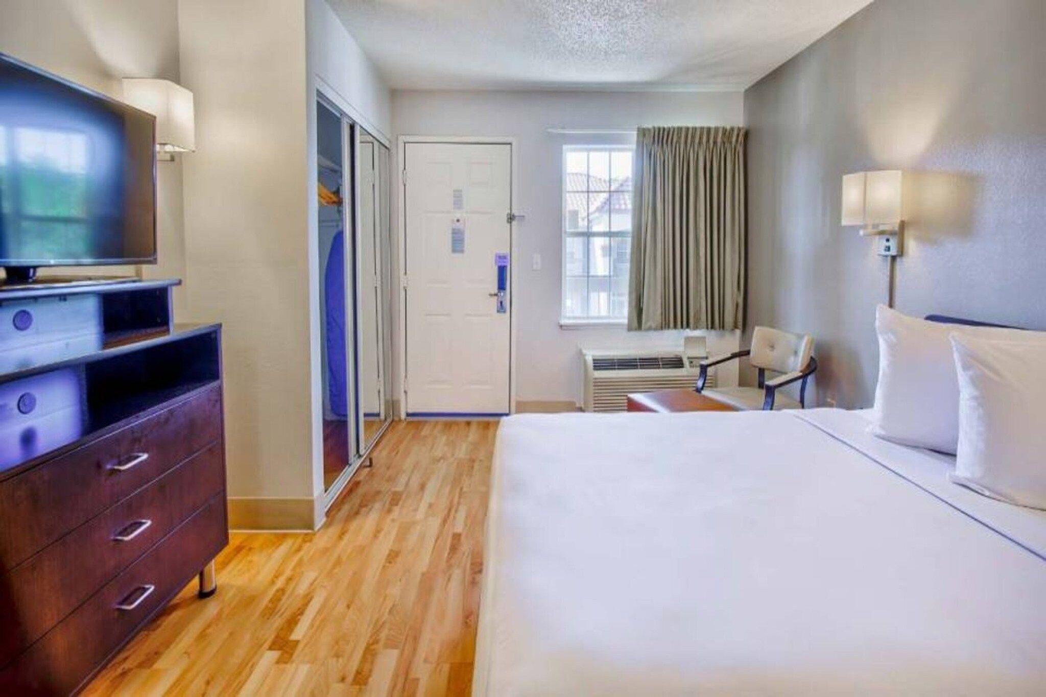 A hotel room with a bed, a TV, a desk, a chair, and a wardrobe.