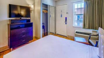 A hotel room with a large bed, a TV on a dresser, a closet with a sliding door, and a window with curtains.