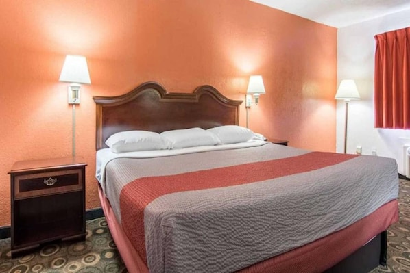 Una habitación de hotel con cabecera de madera, cama con ropa blanca, dos lámparas de noche y una mesita con cajón.