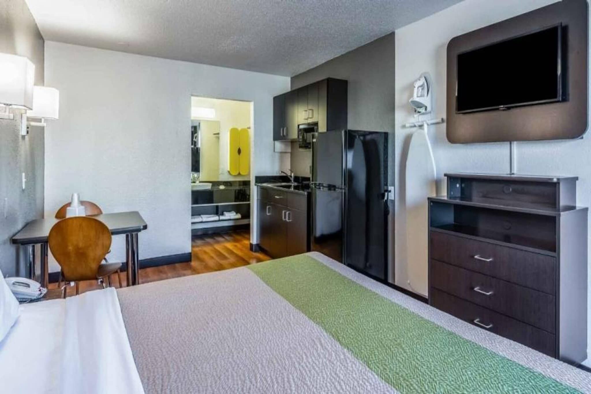 A hotel room with a bed, a desk, a chair, a television, a refrigerator, and a kitchen area.