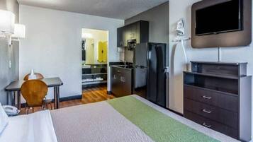 A hotel room with a bed, a desk, a chair, a television, a refrigerator, and a kitchen area.