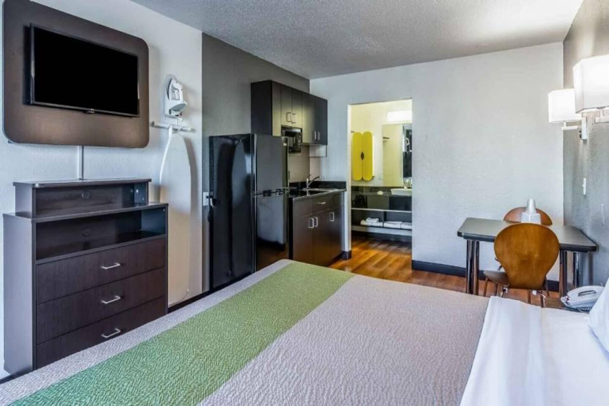 A hotel room with a bed, a desk, a chair, a TV, a refrigerator, and a kitchenette.