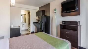 Habitación de hotel con cama, escritorio, refrigerador, televisión y baño visible a través de una puerta abierta.
