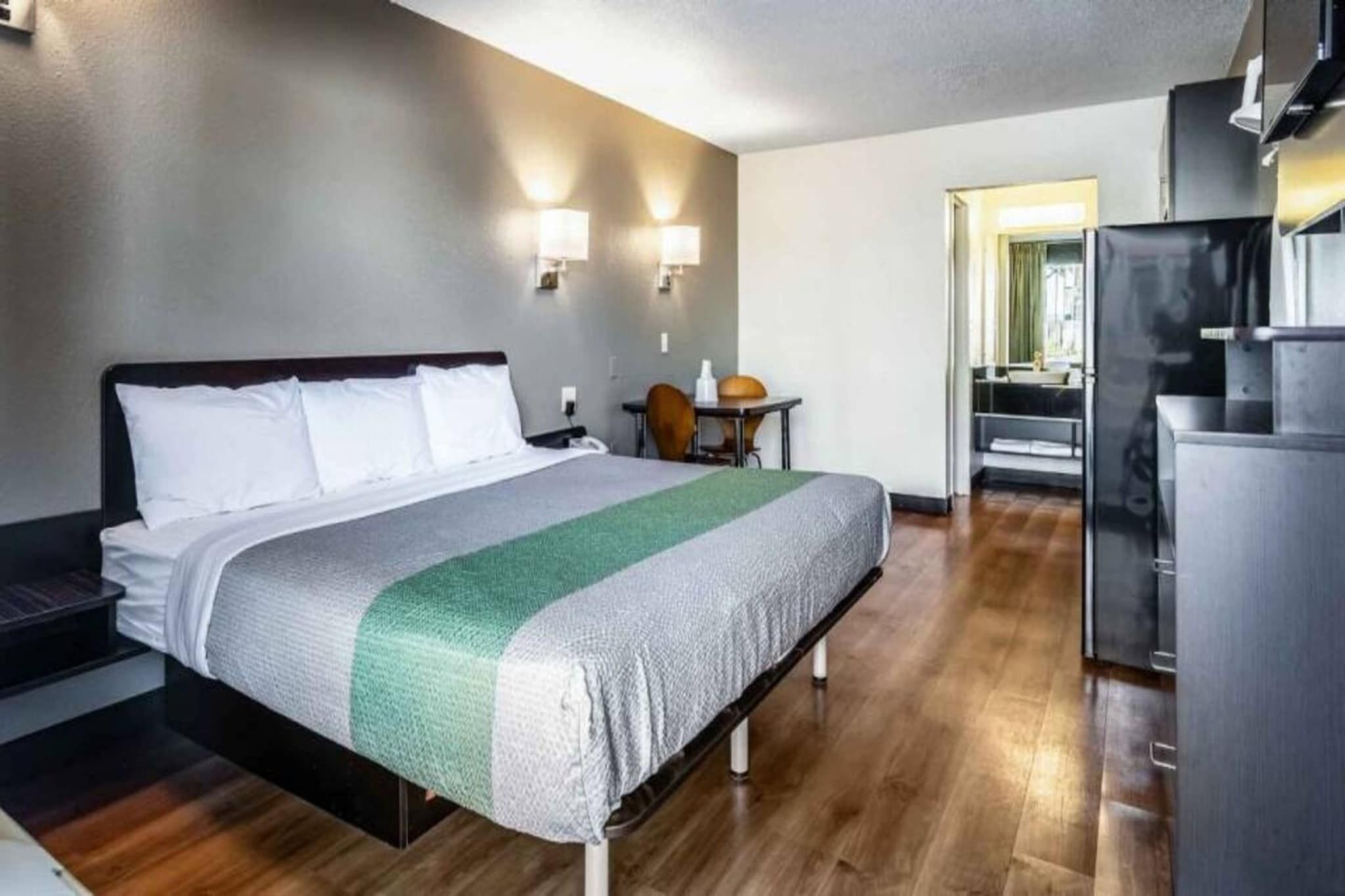 Ein Hotelzimmer mit Bett, Schreibtisch, Stuhl, Kühlschrank und einem durch eine geöffnete Tür einsehbaren Badezimmer.