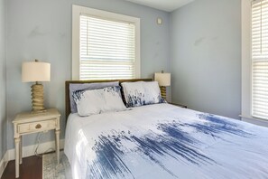 A bedroom with a bed, two bedside tables, a window with blinds, and a wall-mounted light fixture. - Quaint North Campus Bungalow Minutes From Downtown (Austin)