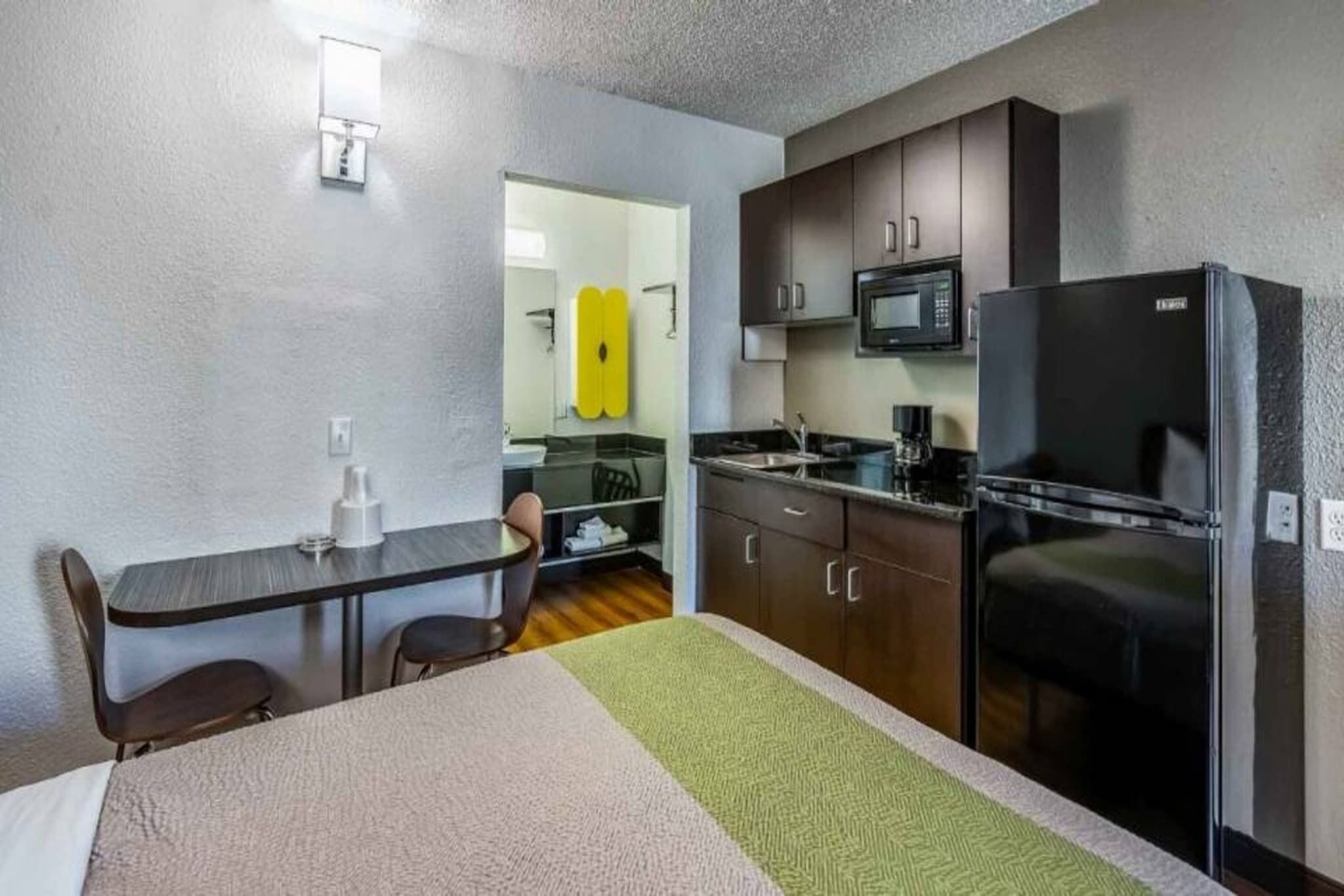 A compact hotel room with a kitchenette, a bed, a desk, and a chair.