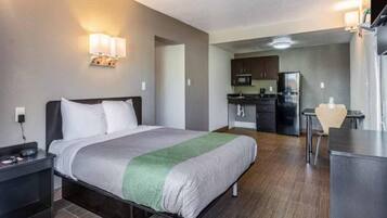 A hotel room with a bed, bedside table, lamp, and a kitchenette area with a refrigerator and microwave.