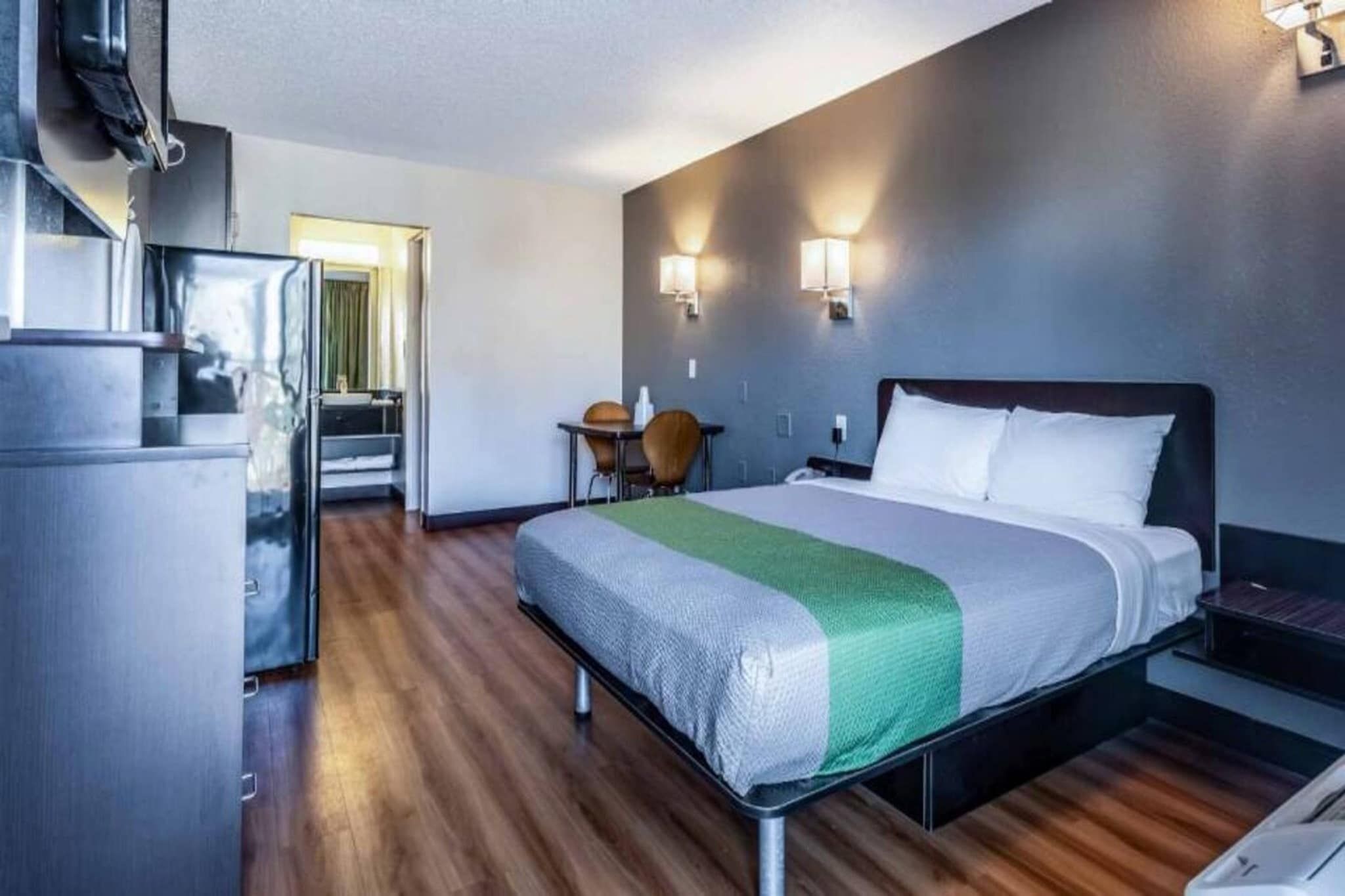 A hotel room with a bed, a desk, a chair, and a kitchenette.