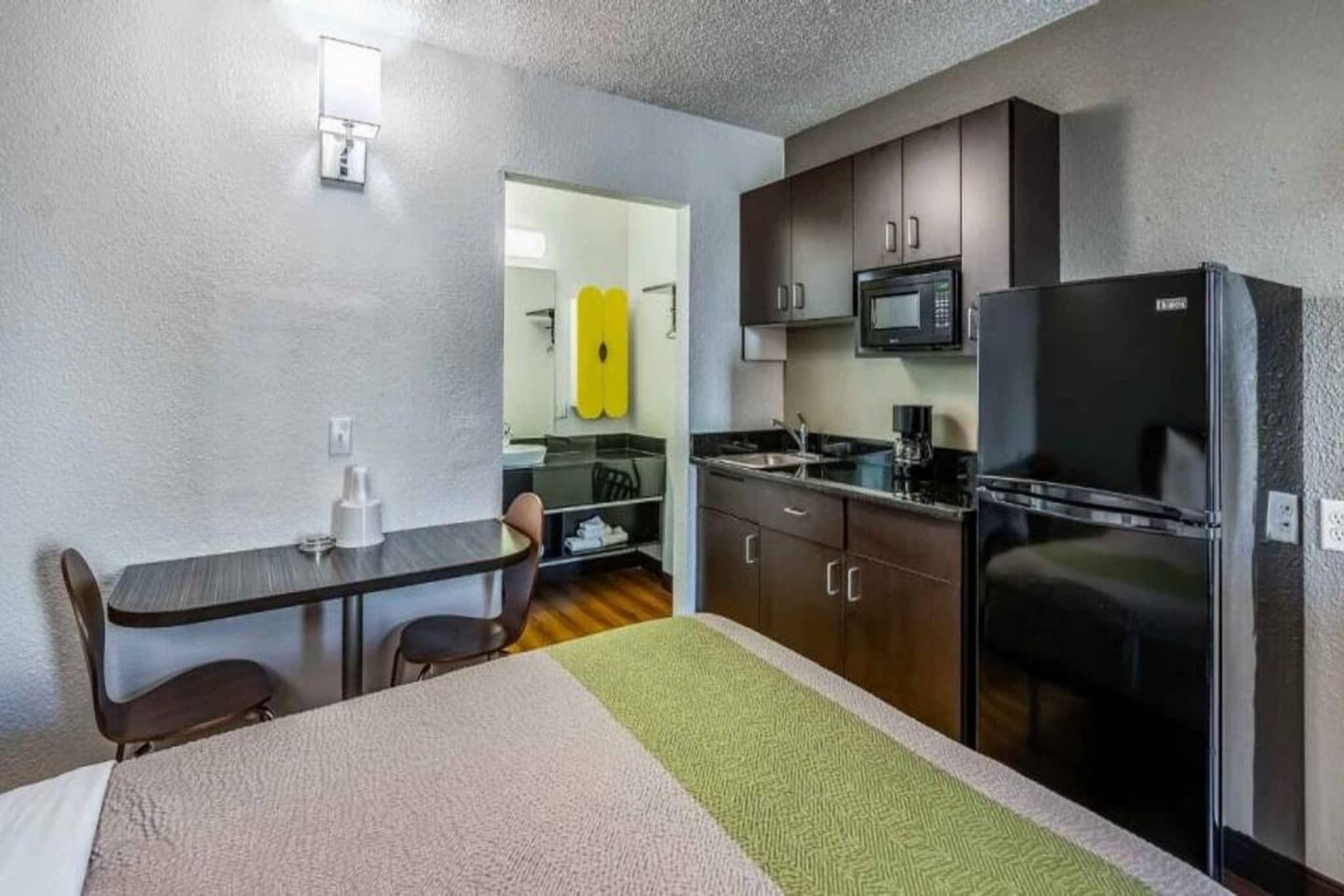 A compact hotel room with a kitchenette, a dining area, and a bed.