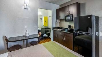 A compact hotel room with a kitchenette, a dining area, and a bed.